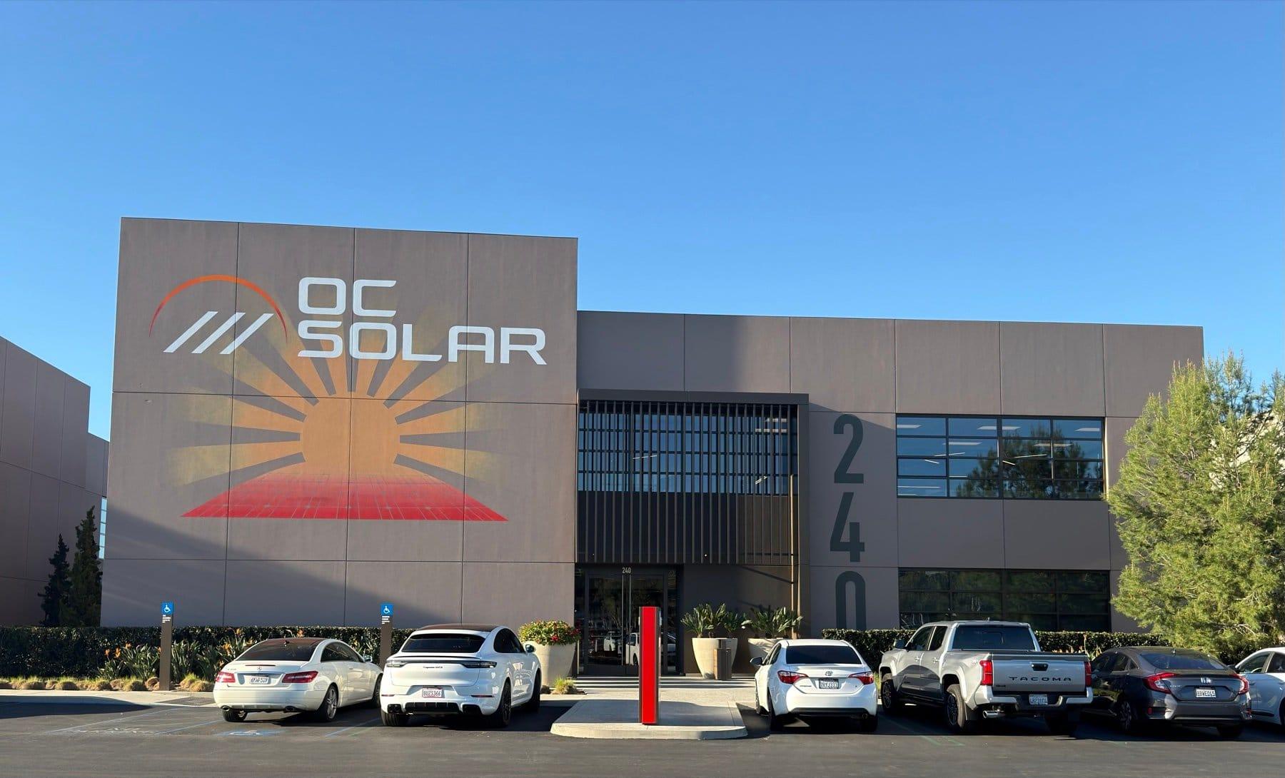 The OC Solar headquarters in Irvine — a two-story building with the OC Solar sunburst logo on the facade and cars parked out front