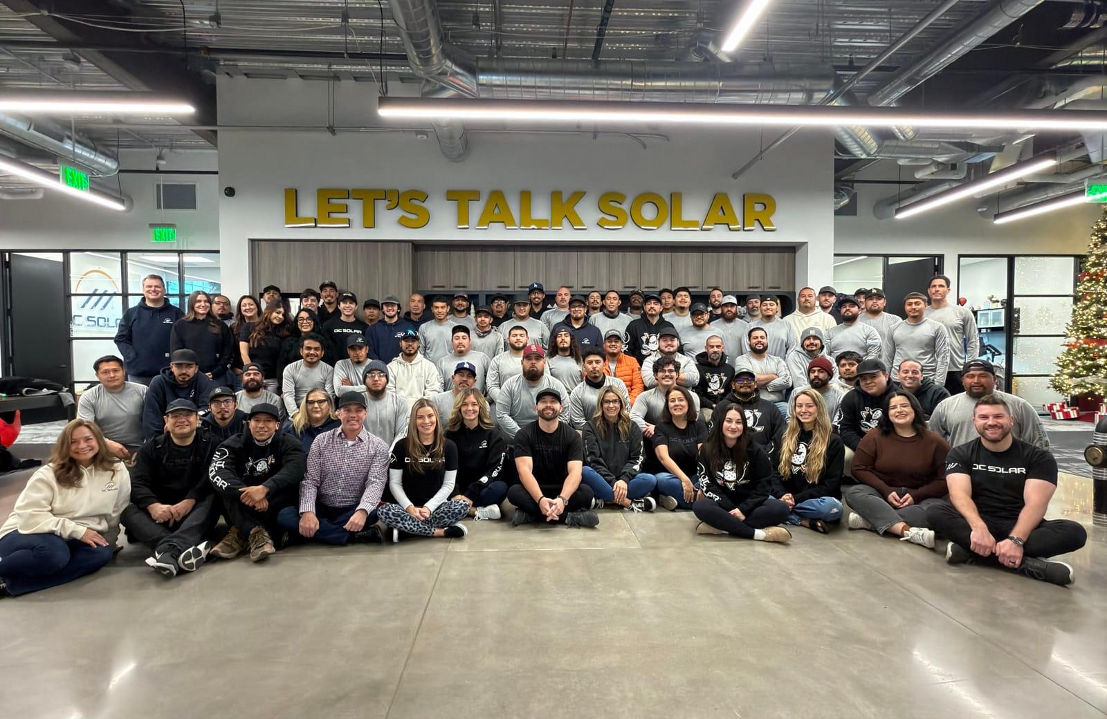 The full OC Solar crew gathered under the Let's Talk Solar sign at the Irvine headquarters