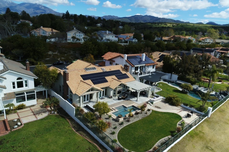 A home seen from above with solar panels installed on the roof and a pool in the backyard